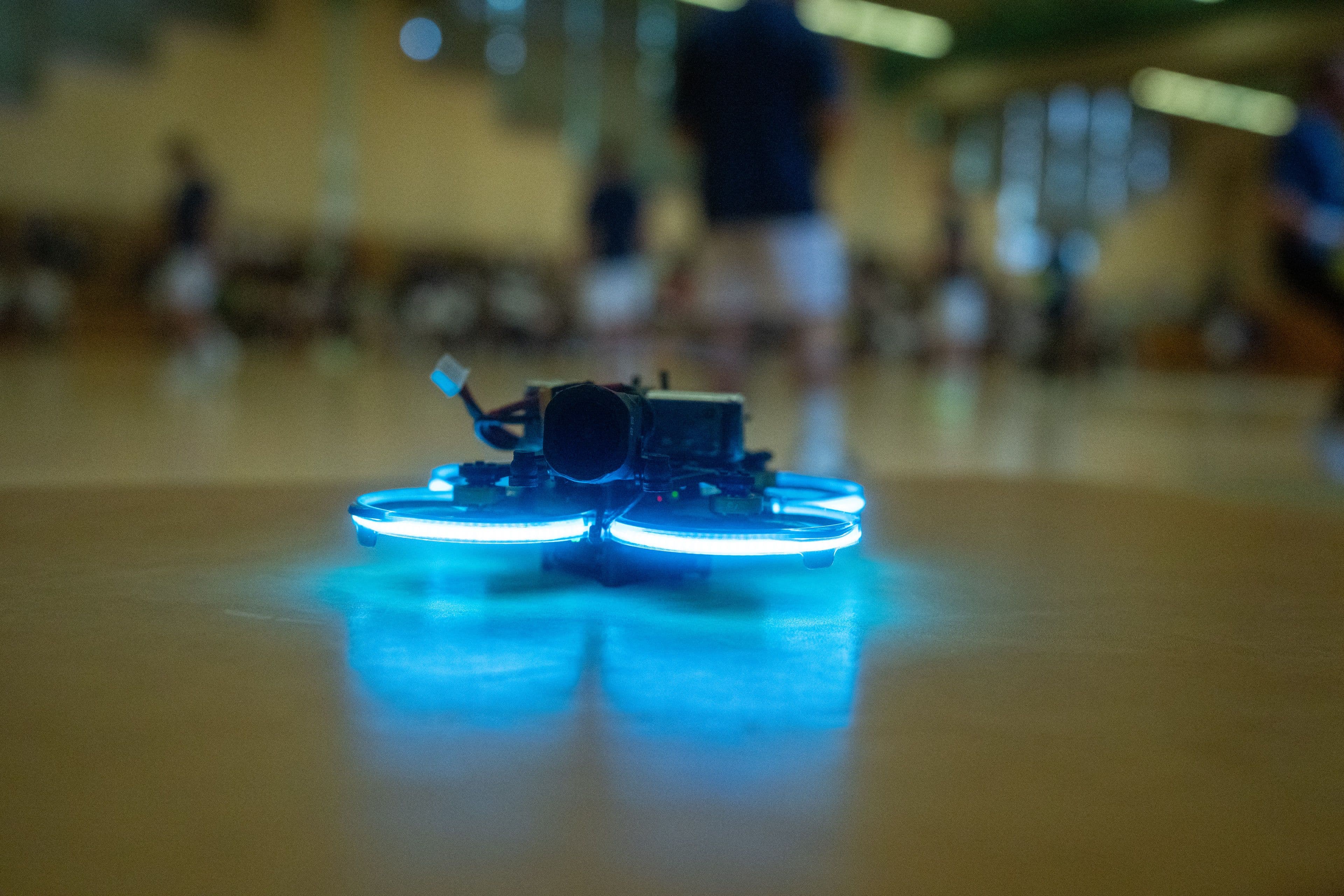 Die FPV-Drohne schwebt dicht über dem Hallenboden, die Rotoren als blauer Lichtkranz