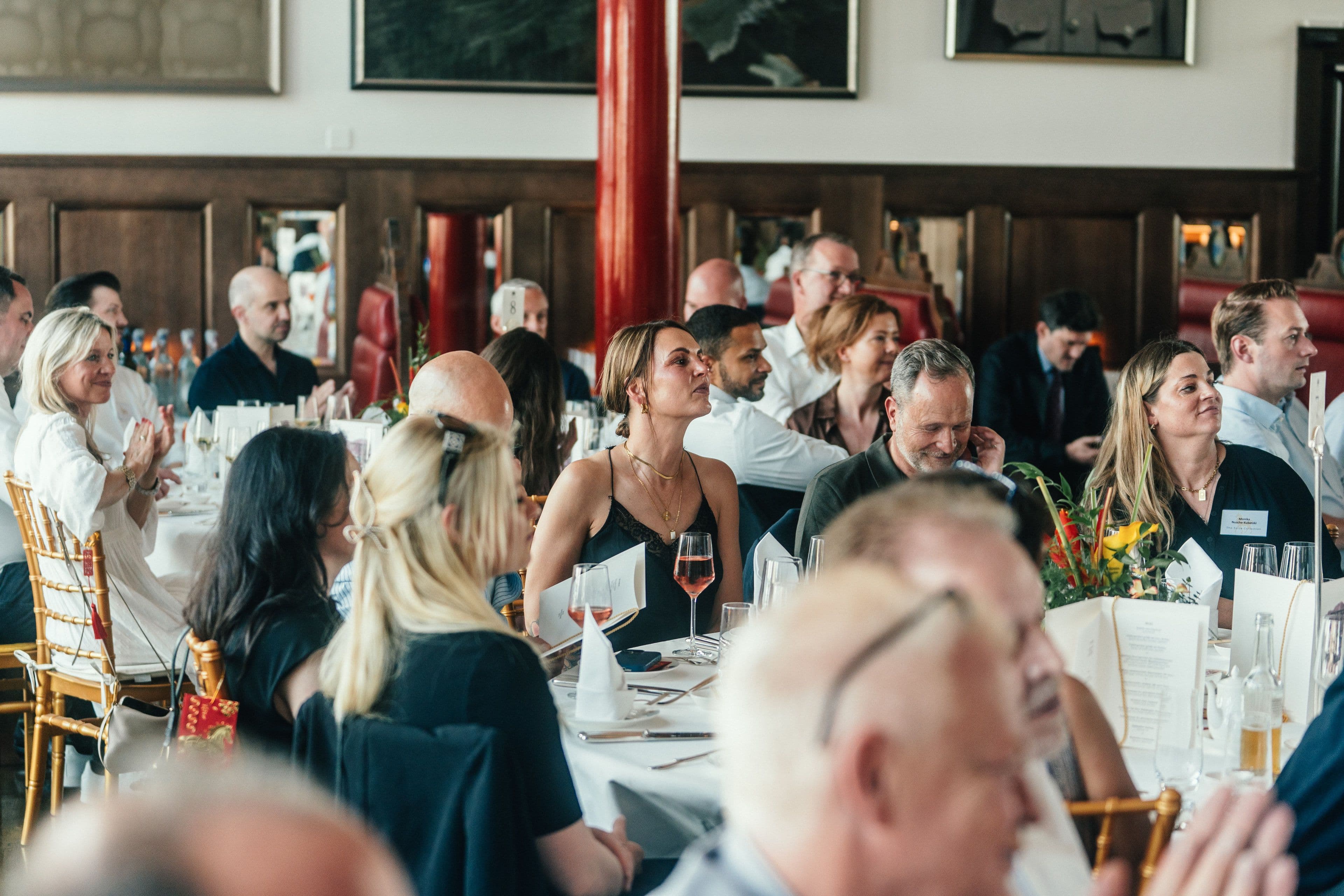 Gäste an der langen Tafel im Gespräch, Weingläser und Menükarten auf dem Tisch