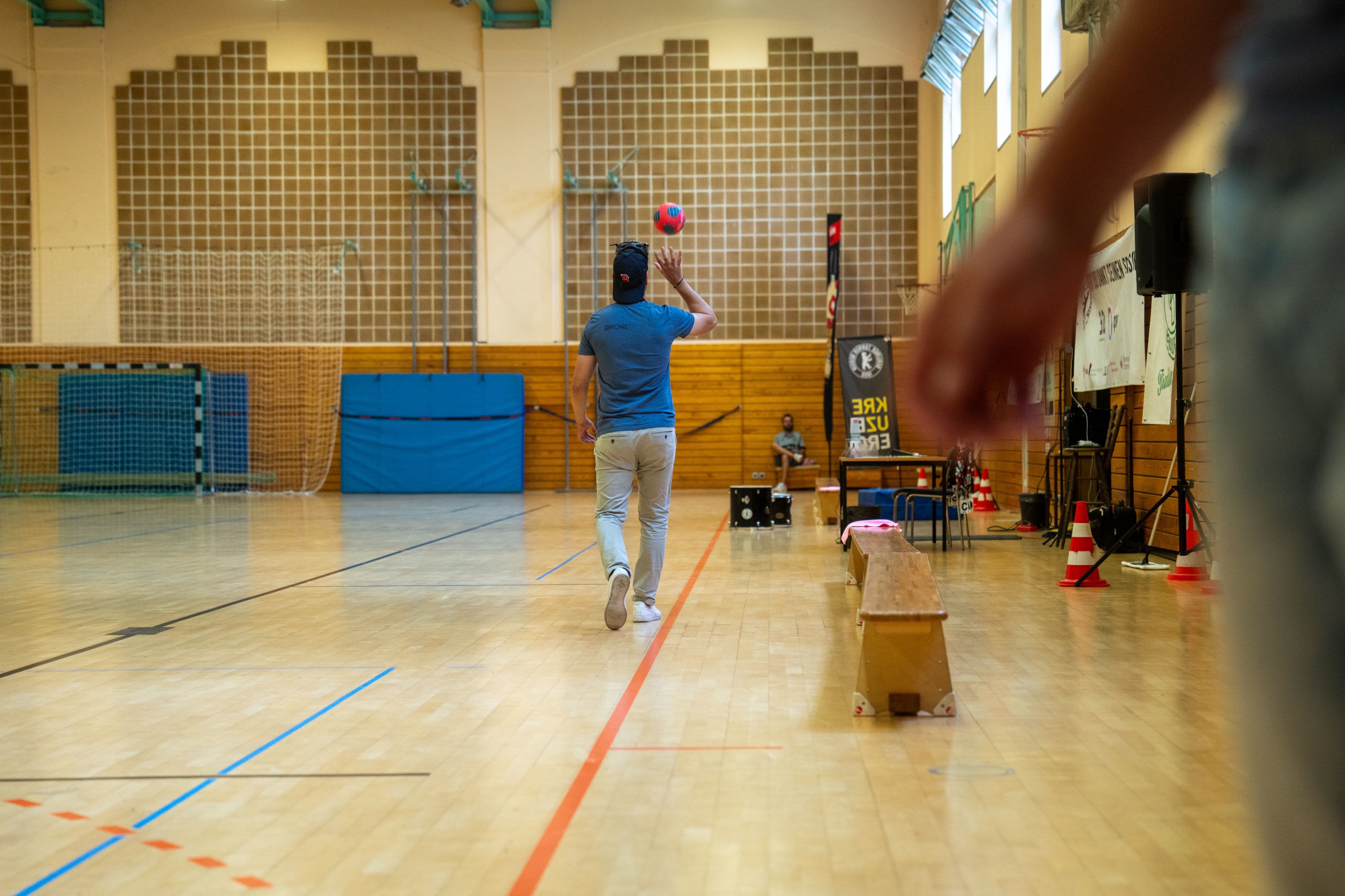 Ein Spieler wirft in der leeren Halle aufs Tor, im Vordergrund die Hand des Drohnenpiloten