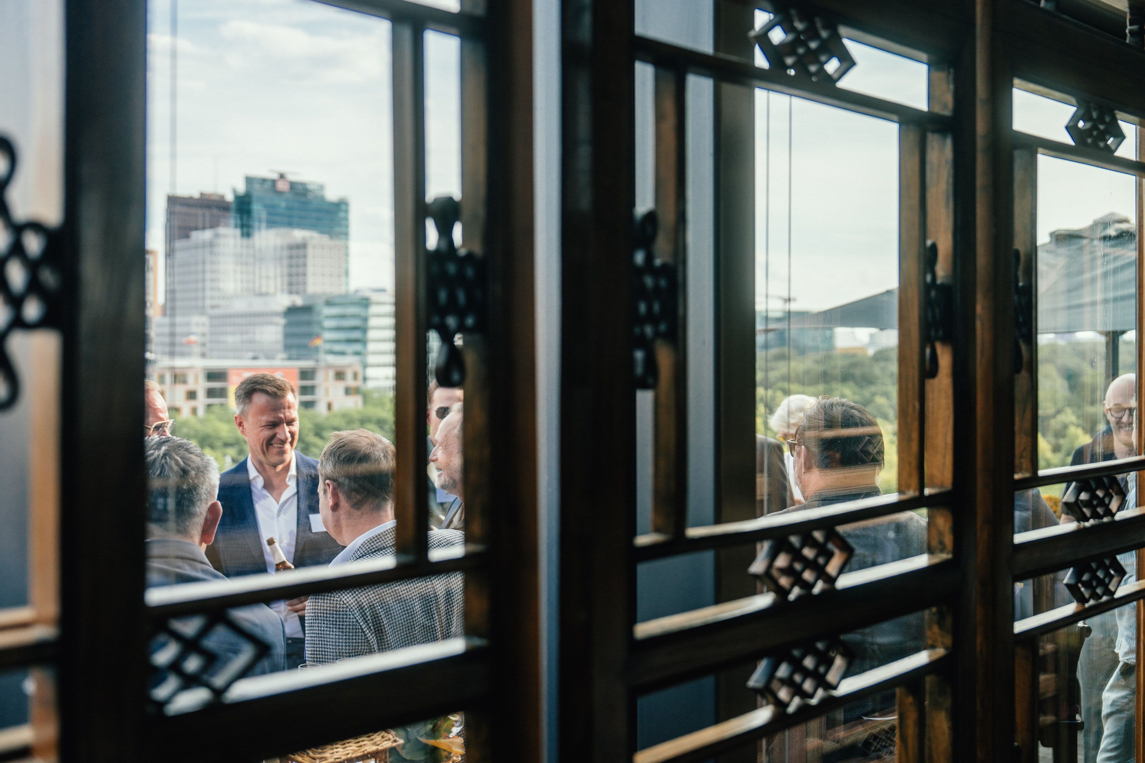 Blick durch ein Gitterfenster auf Gäste beim Empfang, dahinter die Skyline