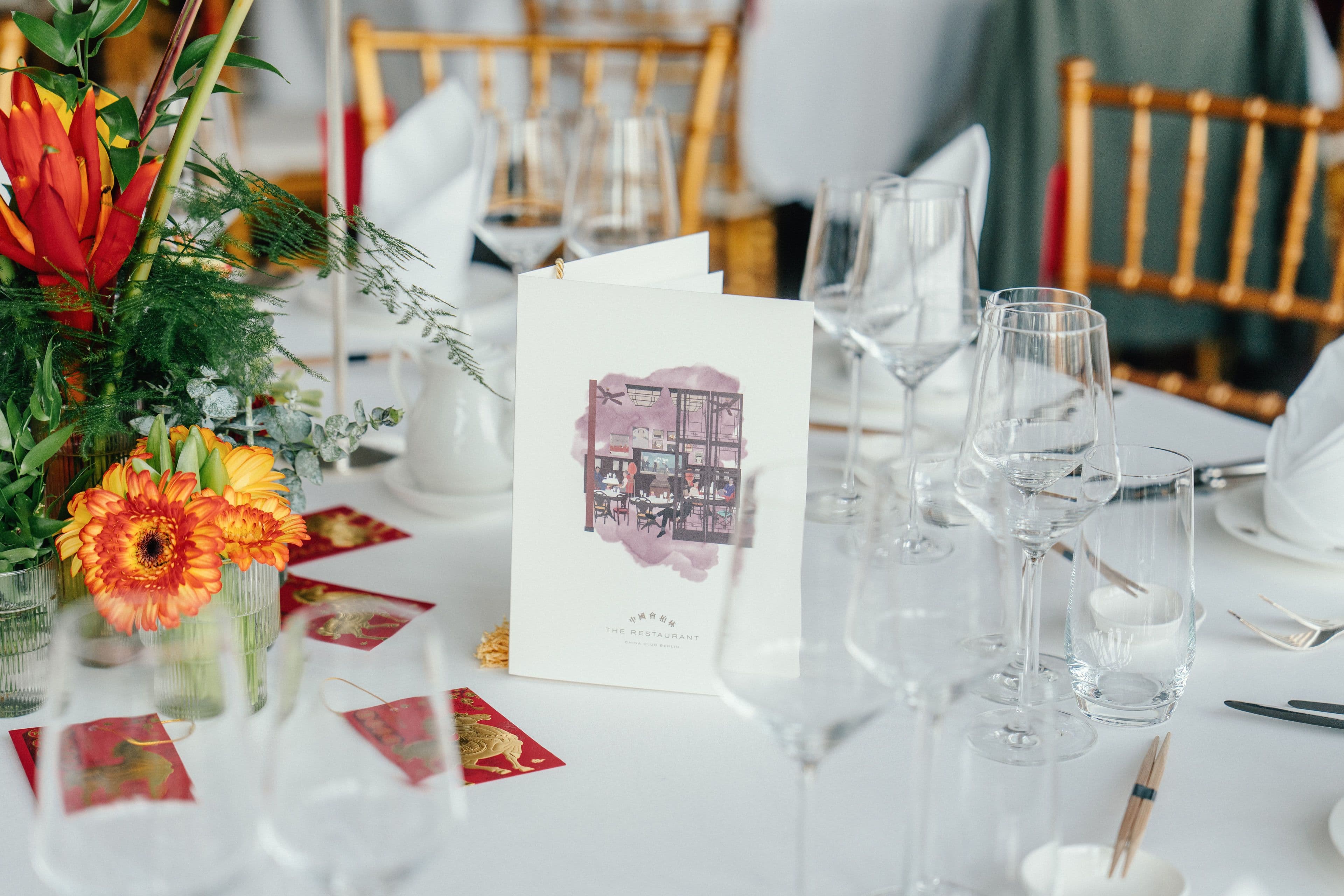 Eine Menükarte zwischen Blumenschmuck und Weingläsern auf dem gedeckten Tisch