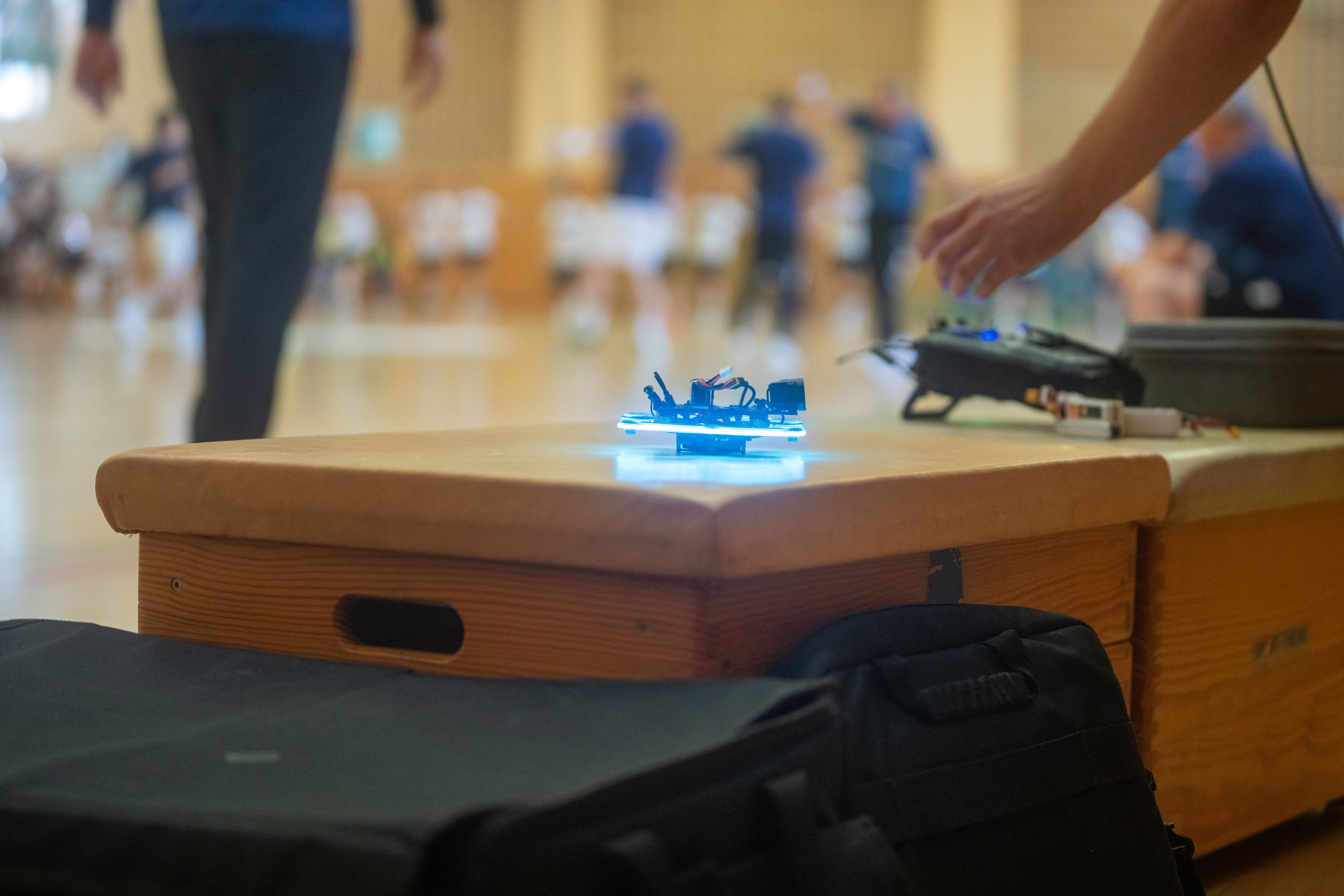 Eine FPV-Drohne mit blau leuchtenden Rotorringen steht startbereit auf einem Sprungkasten